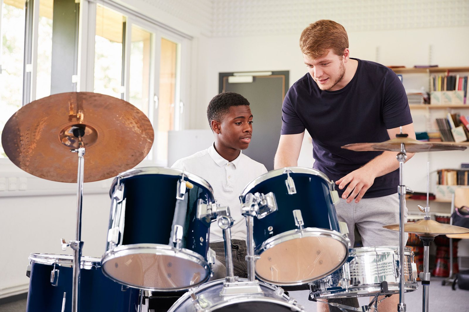 Two teenage boys playing a drum kit in a school music room