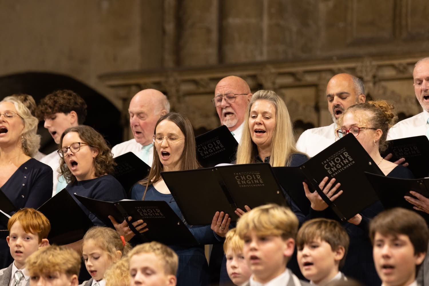 Adults and children singing together from black folders in a church