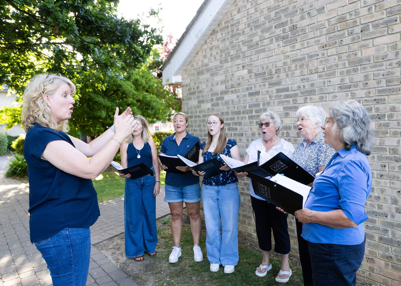 A small group singing outdoors from black folders
