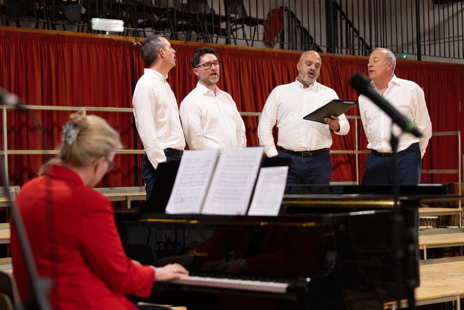 A pianist accompanying singers on a curtained stage